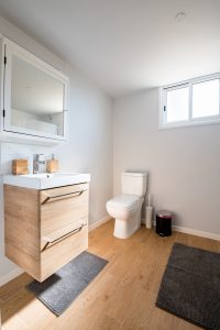 modern bathroom showing the sink, mirror and toilet with wood floors and gray walls